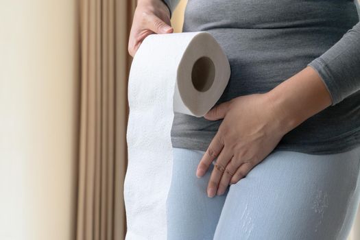 Disorder, Diarrhea, incontinence. Healthcare concept. Woman hand holding her crotch lower abdomen and tissue or toilet paper roll.