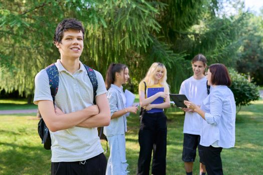 Portrait of male student in park campus, group of teenagers with teacher background. Adolescence, college, high school, education concept.
