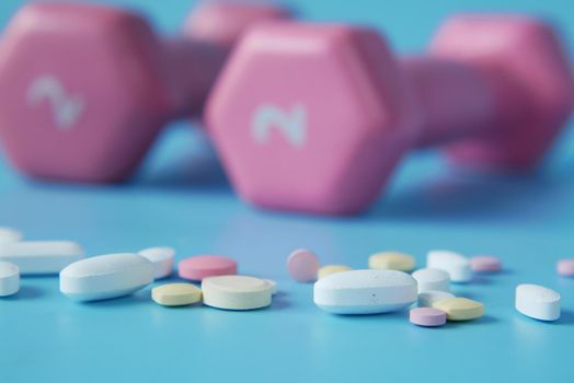 pink color dumbbell and medical pills on blue background .