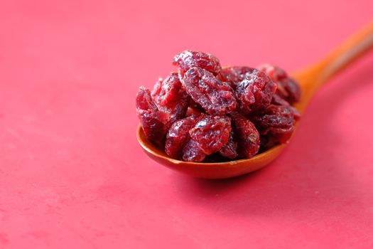dried cranberries on a wooden spoon on red background .