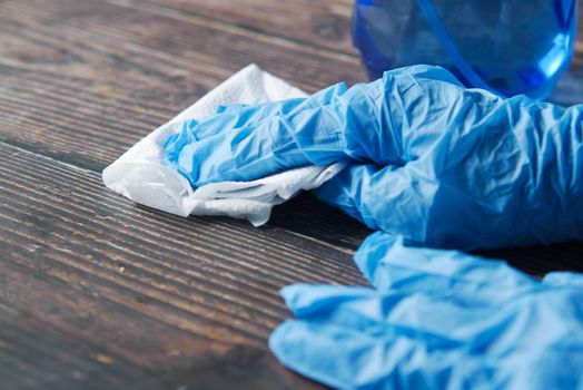 hand in blue rubber gloves cleaning table with towel .