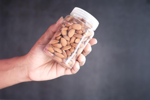holding a jar full of almond against black background .