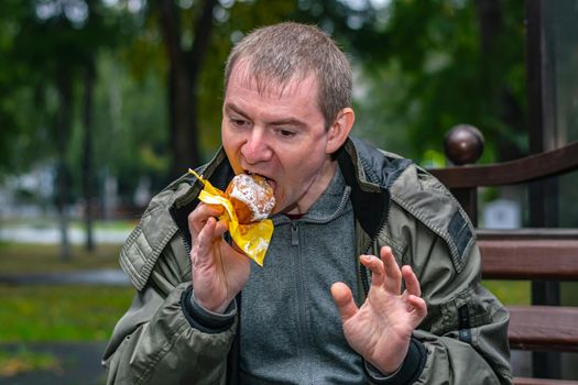 A very hungry man eats with great pleasure a delicious cupcake on the street in the park