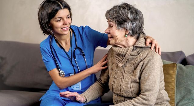 A young nurse takes care of an elderly 80-year-old woman at home, holds her hands . Happy retired woman and trust between doctor and patient. Medicine and healthcare.