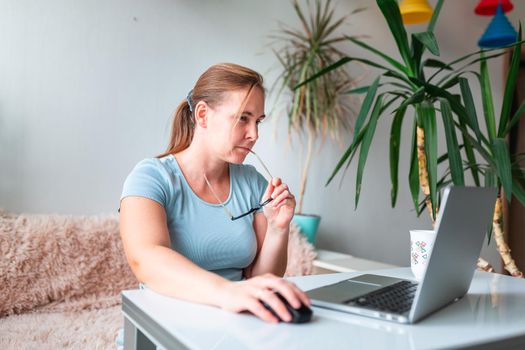Middle age woman sitting at the table at home working using computer laptop. Work from home and stay at home during coronovirus pandemic concept
