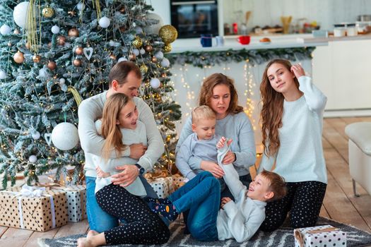 Happy family with four sibilings near the Christmas tree with the present boxes. Christmas family morning, christmas mood concept