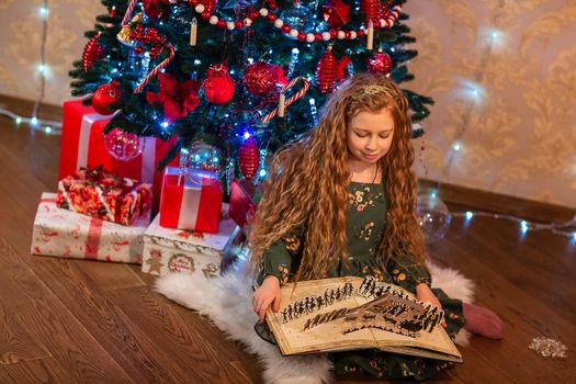 Happy little girl opening the present and reading the book near the Christmas tree Christmas morning, christmas mood concept