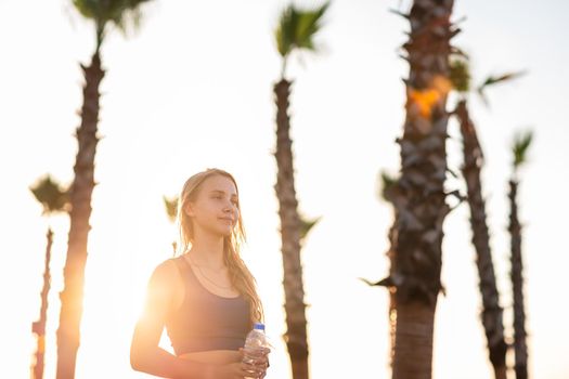 Young girl exercising on seafront line at sunset sunrise. Beautiful girl drinking water while jogging on sea promenade during summer Vacation Meditation Seaside Sea Ocean Holiday Travel