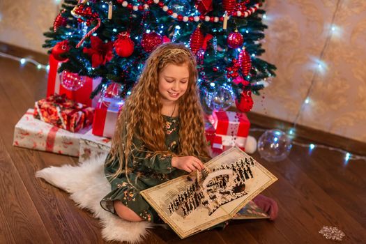 Happy little girl opening the present and reading the book near the Christmas tree Christmas morning, christmas mood concept