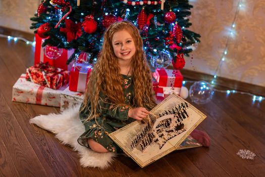 Happy little girl opening the present and reading the book near the Christmas tree Christmas morning, christmas mood concept