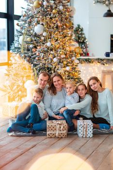 Happy family with four sibilings near the Christmas tree with the present boxes. Christmas family morning, christmas mood concept