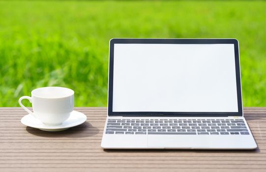 laptop and cofree cup on wood table agent green grass field in countryside