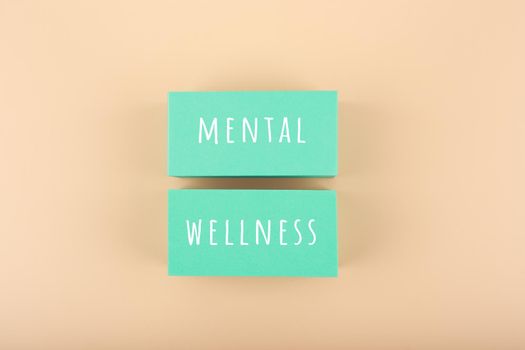 Creative flat lay with aqua blue tablets with written mental wellness text on bright beige background. Concept of world mental health day, mental health assessment and awareness