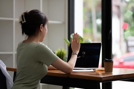 Cropped view of woman waving hand while having video call with laptop computer.