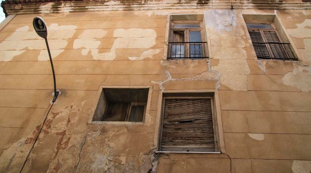 Old house facade with rusty balcony and blind next to vintage streetlight. Novelda village, Valencia community, Spain.