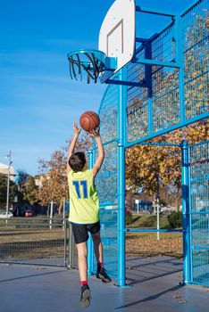 A teenager throwing a basketball into the hoop from behind