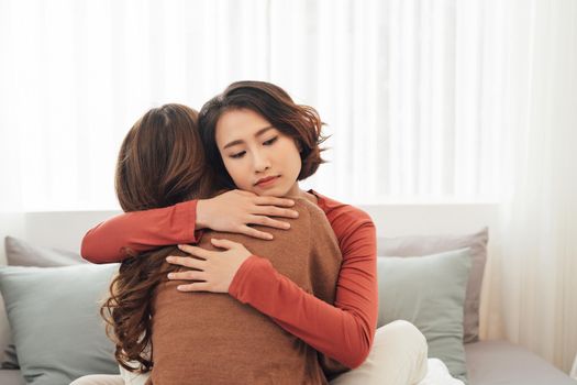 Side view of two sad good friends embracing in a bedroom in a house interior 