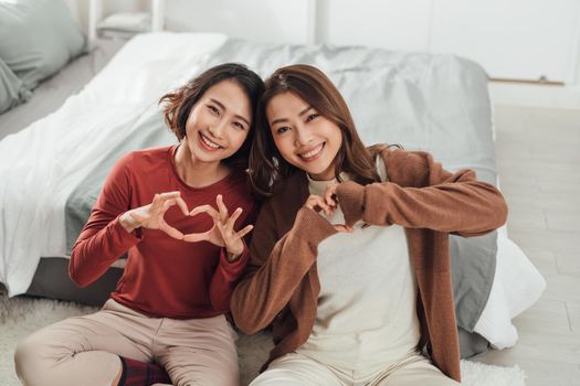 Two young women in bedroom at home lying on bed making heart shape with hands