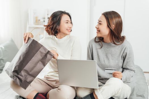 Two female friends chilling at home at using technology shopping online
