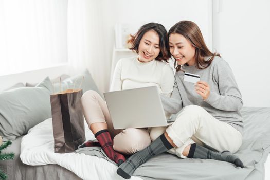 Two young women and best friends doing some online shopping at home with a laptop and a credit card 