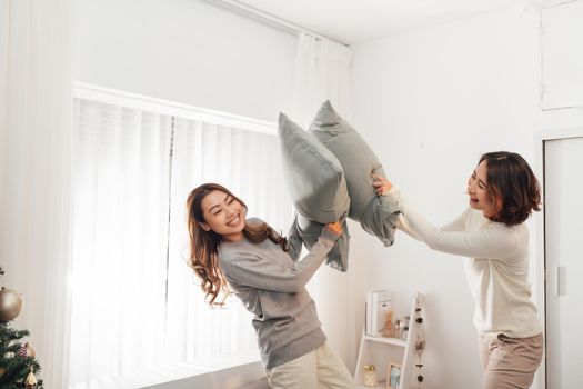 Asian woman with attractive smile while play pillow with friend.