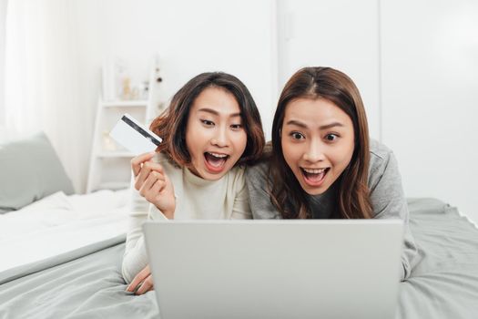 Two happy women shopping online with credit card and laptop at home 