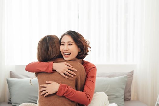 Two happy friends or sisters hugging sitting on a couch in the living room at home