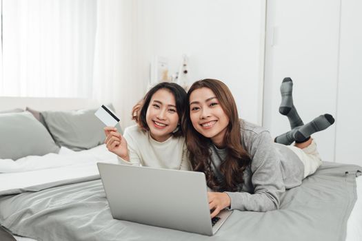 Happy relaxed young female friends doing online shopping through laptop and credit card at home