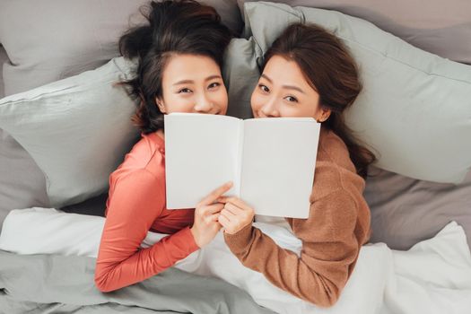 Two women lying on bed and reading book