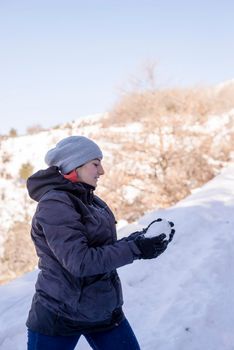 Young woman in the snow mountains landscape on holiday holding natural soft white snow in her hands to make a snowball