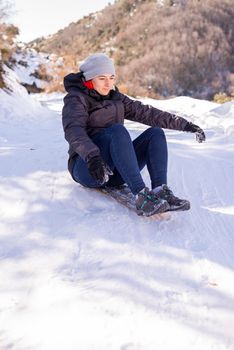 Lifestyle portrait of pretty young woman sliding down hill on snow saucer sled outdoors in winter. Funny face. Emotional photo. Winter sports with snow. Sledding - fun in the mountains. Winter fun