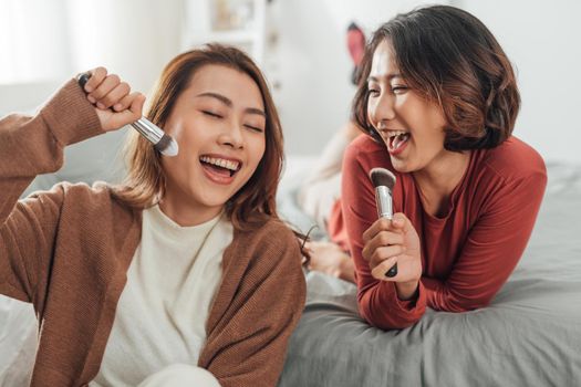 blissful friends fooling around singing while doing makeup in bedroom.