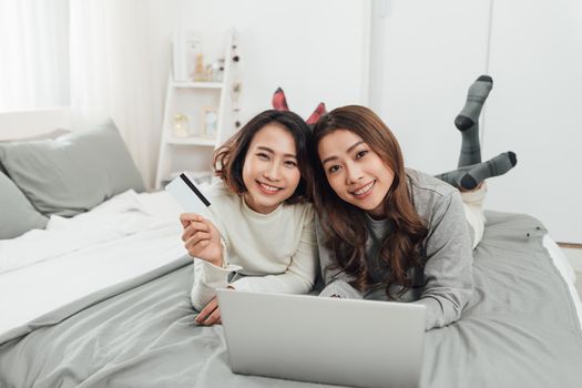 Asian woman friends sitting in living room using digital tablet for online shopping with credit card together