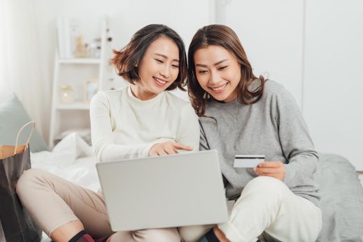 Two excited women shopping online with credit card and laptop at home