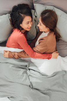 wo young women spend time next to each other, lying on the bed and laughing.