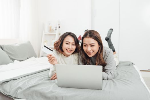 Two happy women shopping online with credit card and laptop at home 