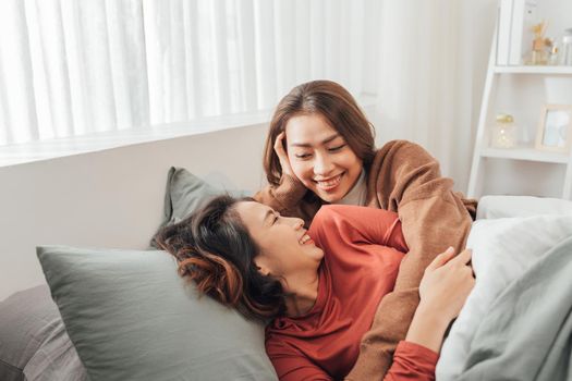 wo young women spend time next to each other, lying on the bed and laughing.