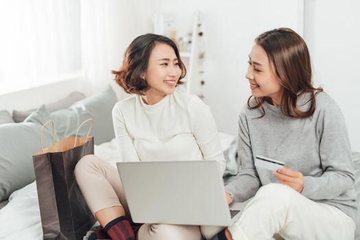 Two happy roommates buying together on line with credit card and a laptop at home