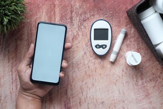 holding a smart phone and diabetic measurement tools on table .