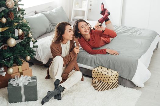 Cheerful young female friend with brush as mic singing while sitting on the bedwhile resting on bed during makeup