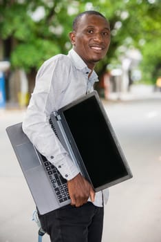 young man standing in shirt with laptop watching camera smiling.