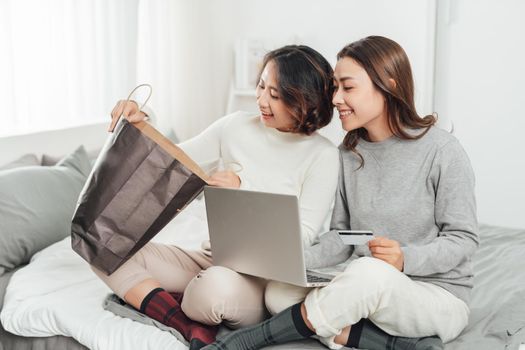 Two excited women shopping online with credit card and laptop at home