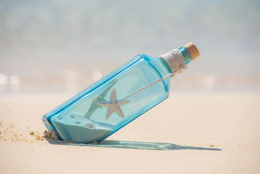 Closeup of blue glass still life on tropical island sandy beach paradise with ocean in background concept message in a bottle