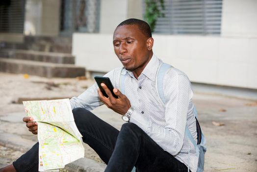 young man sitting in shirt with map in hand watching mobile phone with strange air.