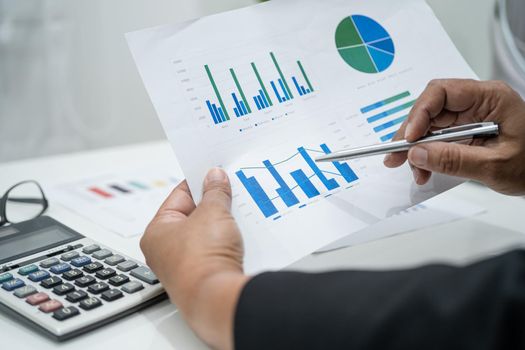 Asian accountant working and analyzing financial reports project accounting with chart graph and calculator in modern office, finance and business concept.