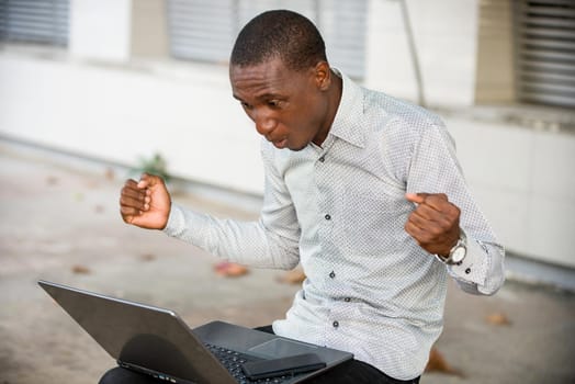young man sitting in shirt looking at laptop, surprised.