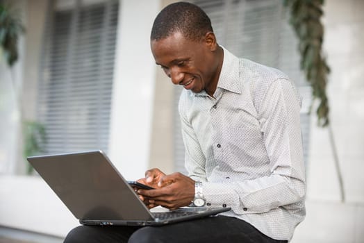 young man sitting in shirt looking at mobile phone smiling.