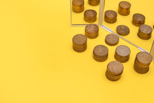 concept of profit growth. a stack of coins near the mirror on a yellow background. copy space. Ukrainian hryvnia