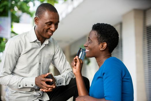 Portrait of a beautiful girl holding and showing a credit card while discussing with a friend of work