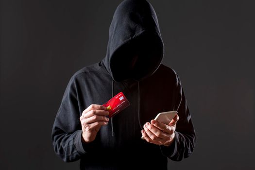 front view male hacker holding smartphone credit card. High resolution photo